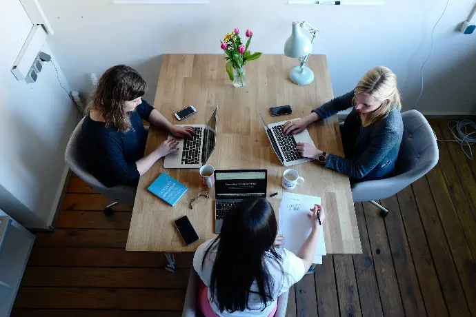 trois femmes assises autour d'une table utilisant des ordinateurs portables